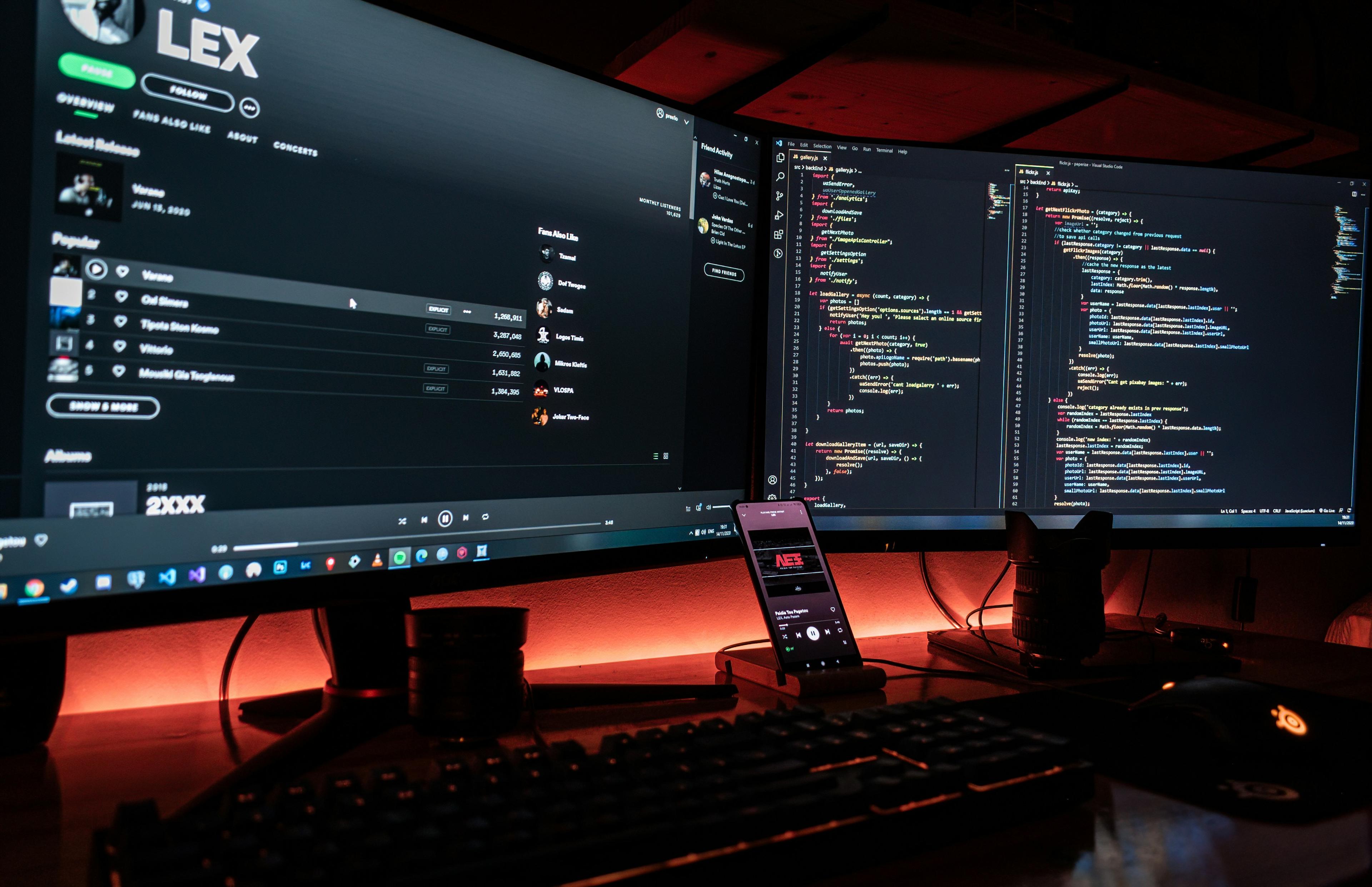 Foto de um setup de um desenvolvedor web com dois monitores, celular, notebook e um teclado mecânico